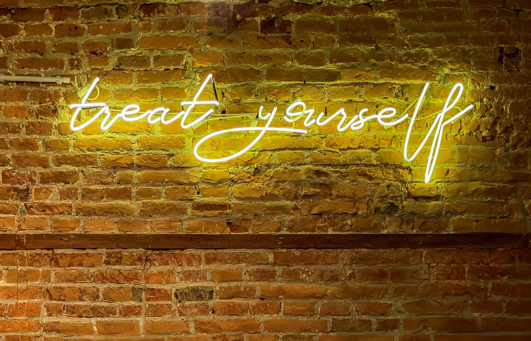 neon sign with the words treat yourself on a brick background