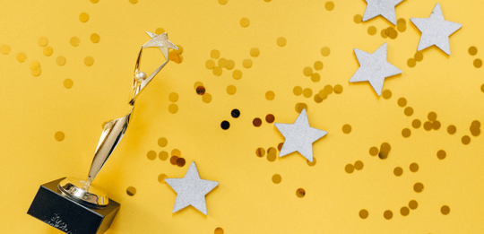 yellow background with a small trophy, stars and confetti for an award