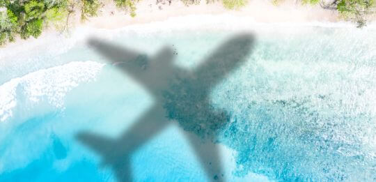 shadow of a. plane flying over the blue sea and sandy beach